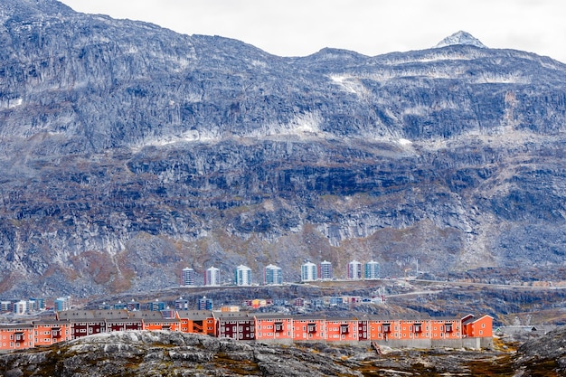 Rows of colorful modern Inuit houses among mossy stones with grey steep slopes of Little Malene mountain in the background Nuuk Greenland