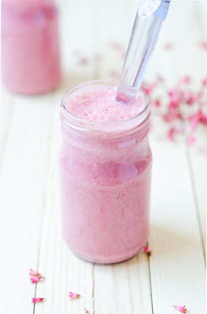 Roze aardbei Smoothie in retro pot met paarse bloemen op de achtergrond op lichte rustieke planken.