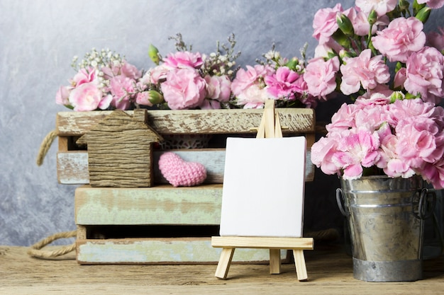 Roze anjerbloemen en leeg canvasframe op schildersezel het schilderen