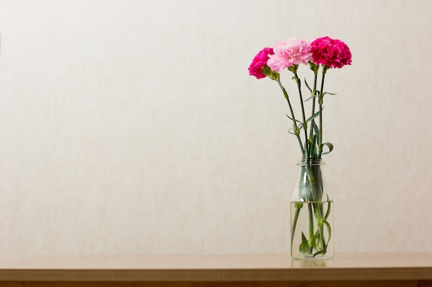 Roze anjerbloemen in duidelijke fles op oud hout