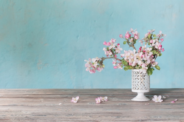 Roze appelbloemen in vaas op blauwe oude muur