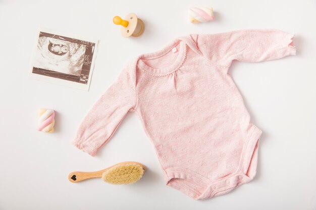 Foto roze baby onesie met echografie foto; fopspeen; heemst; penseel op witte achtergrond