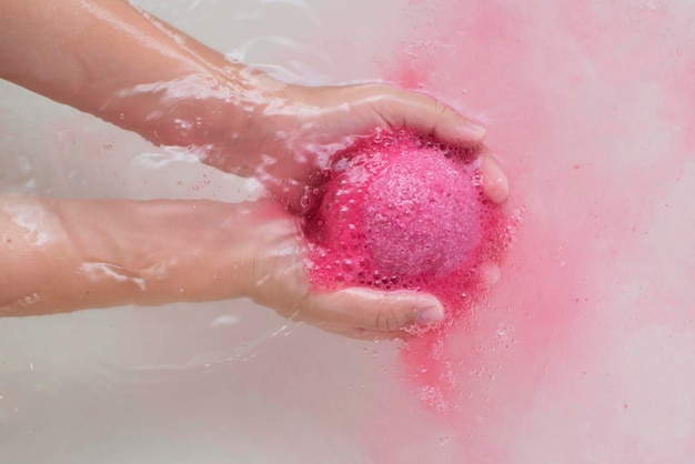 Roze bath bomb in haar handen, schuimend in het water, close-up. Een plek om te kopiëren.