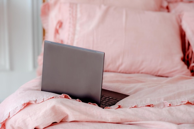 Roze bed met prachtig roze verfrommeld linnengoed in een witte slaapkamer Kantoorwerk op afstand werken vanuit huis op bed Computer gebruiken Afstandsonderwijs online onderwijs en werk