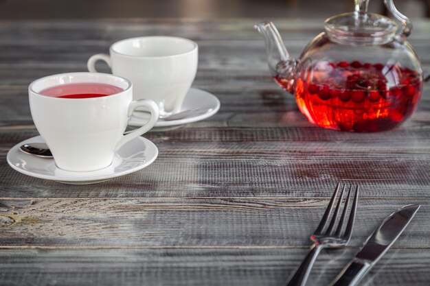 Roze bes rode theepot, witte kopjes, bestek op grijze houten achtergrond