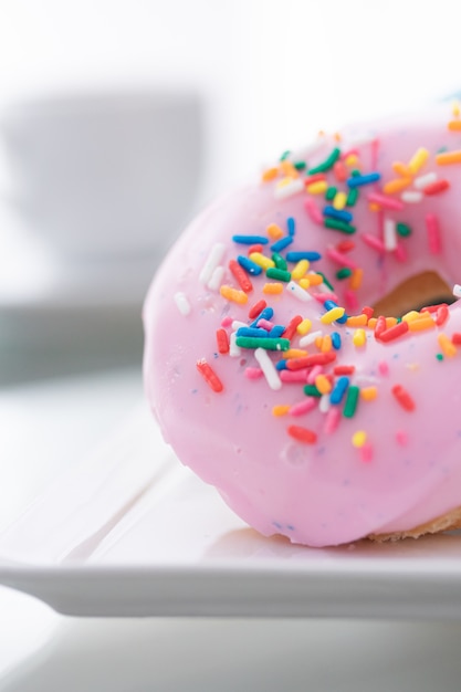 Roze, blauwe en chocolade hagelslag donuts op een witte plaat en een kopje koffie op een licht.