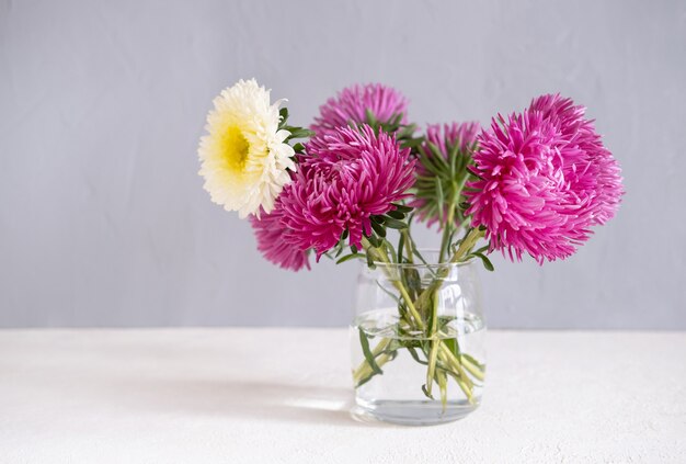 Roze Bloemen In Een Vaas Op Een Witte Tafel Tegen Een Grijze Muur.