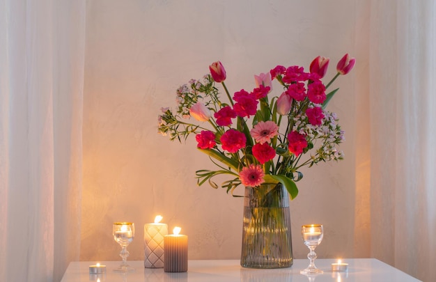 Roze bloemen in glazen moderne vaas met brandende kaarsen in wit interieur