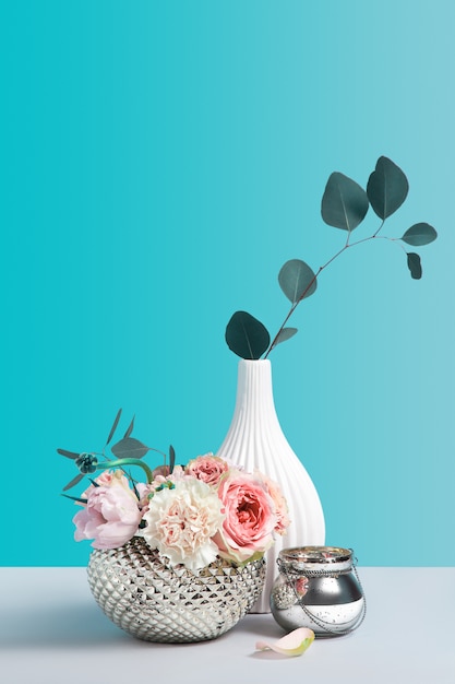 Roze bloemen in metalen stijlvolle vaas op grijze tafel tegen een achtergrond met kleur. Flower shop concept met decor items. Minimalisme stillevensamenstelling met ruimte voor design.