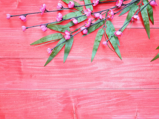 Roze bloesembloemen en groene bamboebladeren op rode houten achtergrond