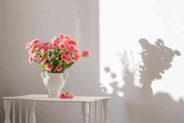 Roze chrysanten in witte vaas op wit interieur