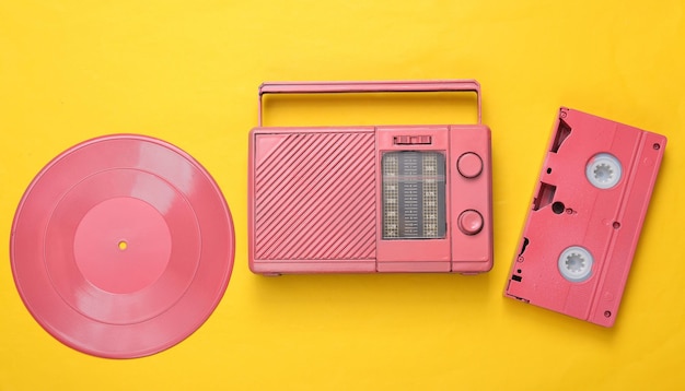 Roze coole radio-ontvanger videocassette en vinyl record op gele achtergrond Minimaal muzikaal concept bovenaanzicht Flat lay