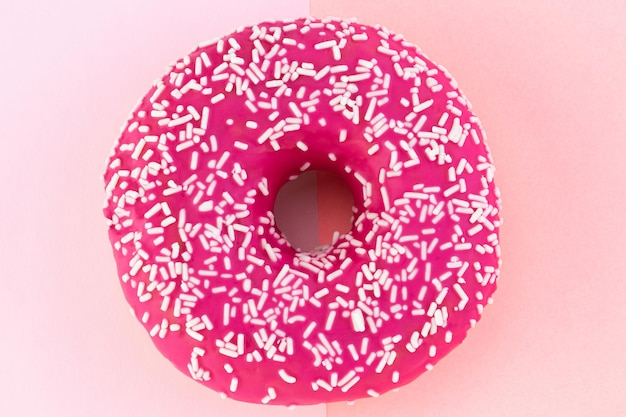 Roze donut met slagroom op pastel roze achtergrond.