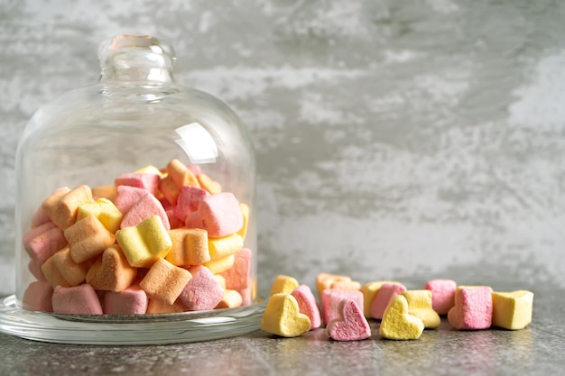 Roze en gele hartvormige marshmallow in glazen bel op grijze betonnen ondergrond