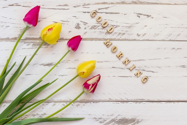 Roze en gele tulpen op houten pagina. lente wenskaart met kopie ruimte. goedemorgen citaat.