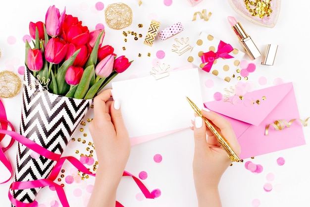 Roze en goud gestyled bureau met bloemen. Vrouwelijke handen houden kaart vast