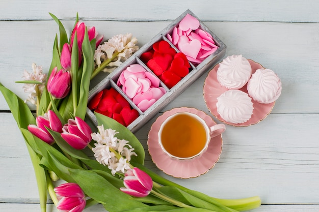 roze en rode harten in een houten doos, een kopje thee en marshmallows en een boeket van hyacinten en tulpen
