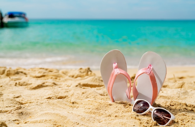 Roze en witte sandalen, zonnebril op zandstrand aan zee. casual mode stijl flipflop en bril aan kust. zomervakantie op tropisch strand.