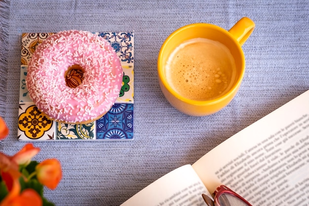 Roze en zoete geglazuurde donut op tafel, een pauze met een boek en een kopje koffie