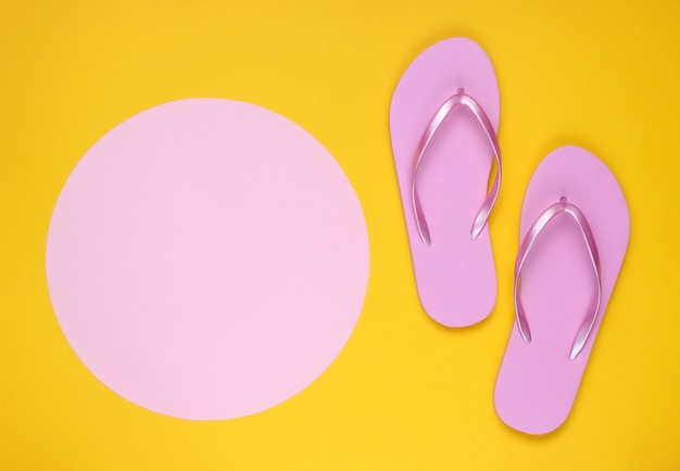 Roze flip-flops op gele achtergrond met roze pastel cirkel voor kopie ruimte. Minimalistische vakantie op het strand-concept. Zomertijd
