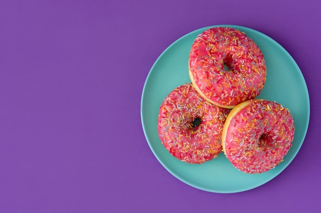 Roze frosted donut met kleurrijke hagelslag geïsoleerd op paars