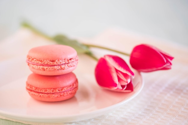 Roze gebaksmakarons in een kom van wit porselein en roze tulpen op wit tafelkleed