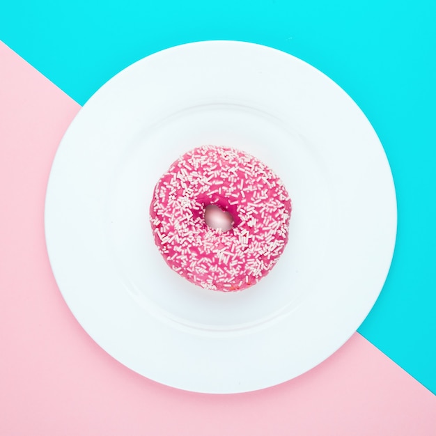 Roze geglazuurde doughnut op gekleurd oppervlak. Plat leggen.