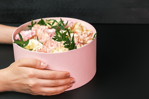 Roze geschenkdoos met een florale compositie in handen van de vrouw op de zwarte achtergrond met kopie ruimte. Cadeau voor Valentijnsdag, Internationale Vrouwendag, 8 maart, Moederdag.