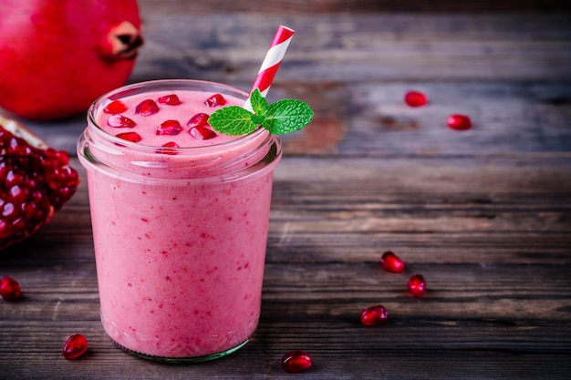 Roze granaatappelsmoothie in een glazen pot met munt en verse zaden op een houten rustieke achtergrond