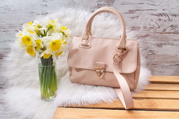 Roze hahdbag en boeket van narcissen op wit bont. Modieus concept