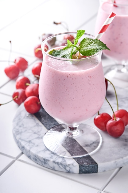 Roze kersensmoothies met verse rode bes, chiazaden, muntgroene bladeren, witte stenen keukenachtergrond. Selectieve aandacht.