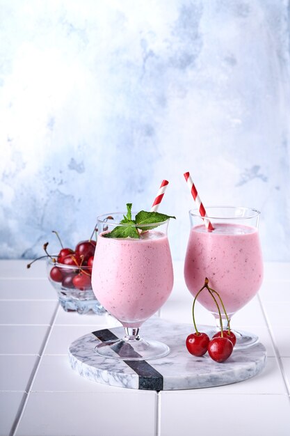 Roze kersensmoothies met verse rode bes, chiazaden, muntgroene bladeren, witte stenen keukenachtergrond. selectieve aandacht.