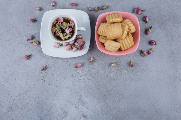 Roze kom met zoete koekjes en kop hete thee op steen.