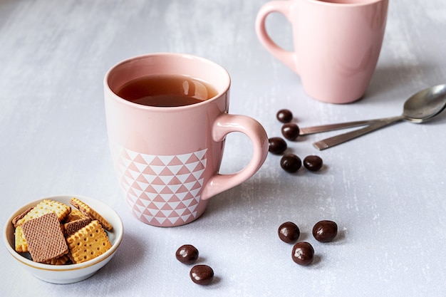 Roze kopje zwarte thee op grijze achtergrond, met koekjes, chocolade en lepels.