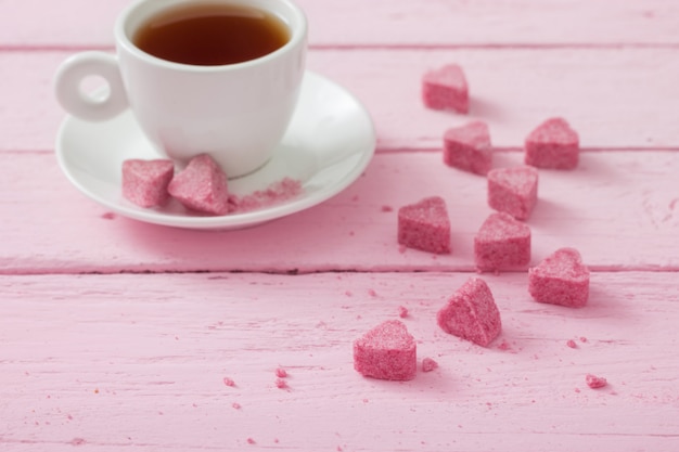 Roze kristalsuiker in de vorm van hart en kopje thee op een houten ruimte