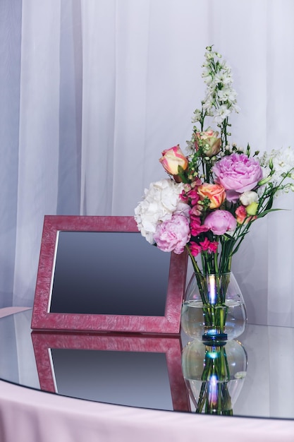 Roze leeg frame en bloemen in een vaas op een spiegeltafel