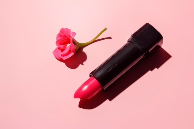 Roze lippenstift met een pelargoniumbloem op een roze achtergrond met een harde schaduw.