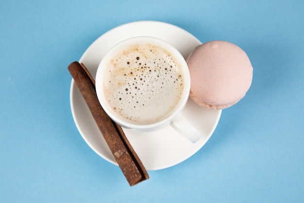 Roze macarons en koffie met kaneel op een blauwe ondergrond