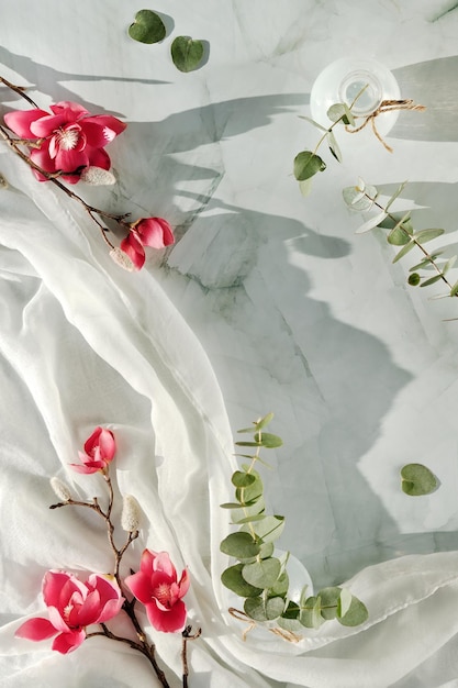 Roze magnoliabloemen en groene eucalyptustakjes op zachte gebroken witte textielsjaal.