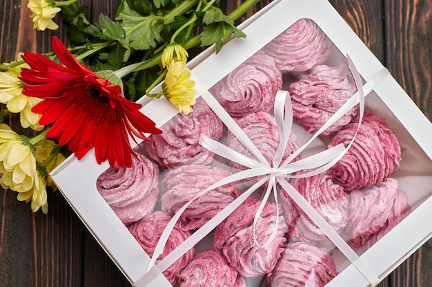 Roze marshmallow, verpakt in een doos met een lint en bloemen, voor een cadeau, op een houten bord