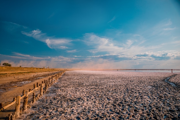 Roze meer en zandstrand met een zee baai onder een blauwe lucht met wolken