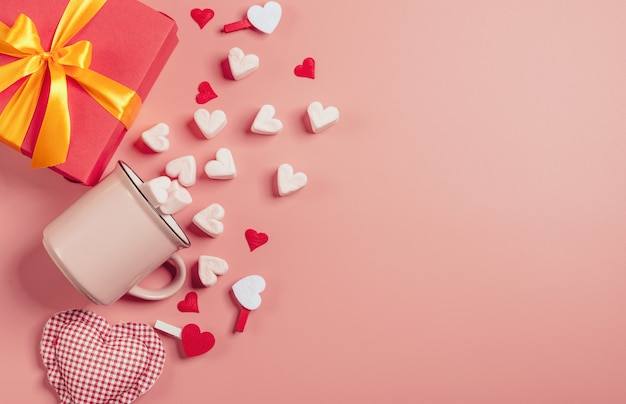 Roze mok op een roze oppervlak gevuld met marshmallows in de vorm van harten. ernaast is een doos met een cadeau voor Valentijnsdag. v