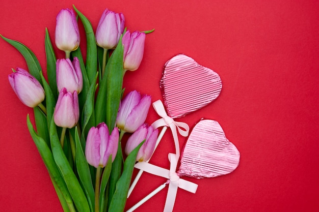 Roze of paarse tulp bloemen en hartvormige chocolade op rode achtergrond. Valentijnsdag of Moederdag concept.