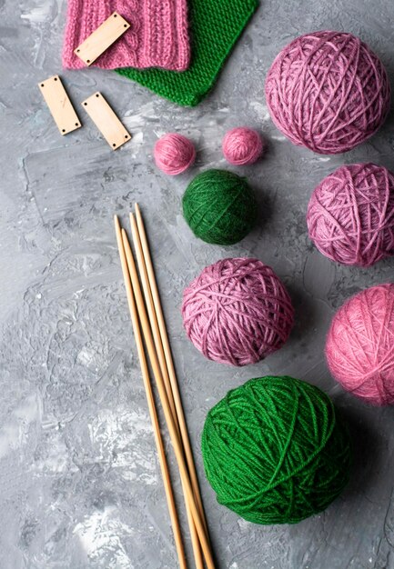 Roze paarse en groene bollen garen met houten breinaalden en tags op grijze achtergrond