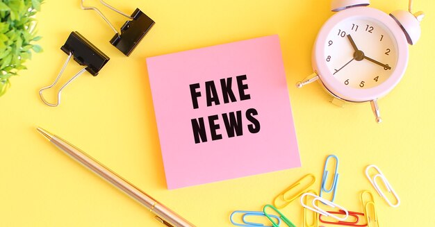 Foto roze papier met de tekst fake news clock pen op een gele achtergrond