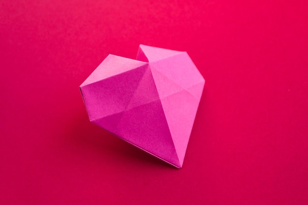 Roze papieren hart origami geïsoleerd op een rode achtergrond