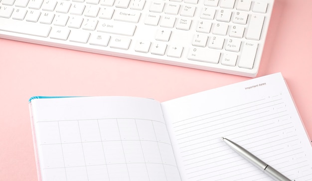 Roze pastel vrouw bureau met toetsenbord en dagboek. Bovenaanzicht met kopieerruimte