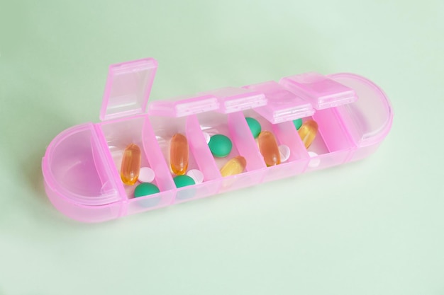 Roze plastic organizer voor pillen en vitamines op een lichtgroene achtergrond