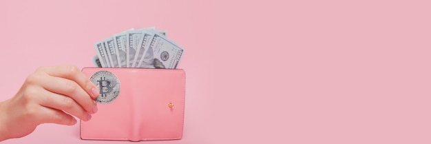 Roze portemonnee met dollars en bitcoin in de hand van de vrouw op een roze met kopie ruimte.