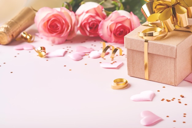 Roze rozen bloemen, champagne, cadeau, gouden linten en confetti rode harten op roze achtergrond. Bovenaanzicht plat lag met ruimte voor uw groeten. Valentijnsdag achtergrond en wenskaart.